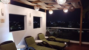 A rooftop lounge with green cushioned chairs, a view of the city at night, and decorative hanging lights. - Bleu Balam • Quiet • Pool • Zazil-Ha • 1 Block to 5th Ave (Playa del Carmen)