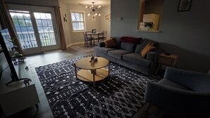 Una sala de estar con sofá, sillón, mesa de centro y una alfombra estampada.