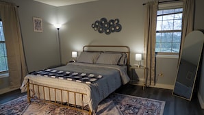 Un dormitorio con cama, lámparas de noche, alfombra, decoración en la pared y una ventana con cortinas.