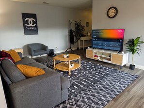 Moderni olohuone, jossa on harmaa sohva, pieni pyöreä sohvapöytä, televisio ja koristeellinen kasvi.