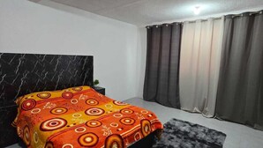 Un dormitorio con una cama, cabecera de mármol, cortinas grises y una alfombra gris.