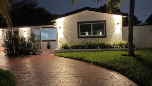 Una casa moderna con vialetto in pietra, illuminazione esterna e una palma.