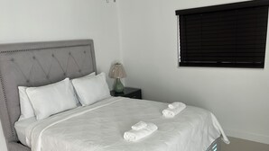 Un letto rifatto con precisione, con una testiera grigia, biancheria bianca e due asciugamani arrotolati ai piedi.