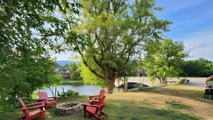 A lakeside outdoor seating area with Adirondack chairs and a fire pit. - 2 Condos on Ausable River w/ Dock & Backyard (Wilmington)