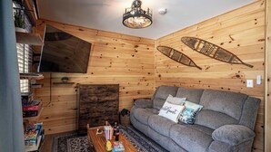 A cozy room with a wooden interior, a sofa with a cushion, a table with snacks, and a ceiling light fixture. - 2 Condos on Ausable River w/ Dock & Backyard (Wilmington)