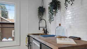 A kitchen with white subway tiles, a wooden countertop, a window, and hanging plants. - 2 Condos on Ausable River w/ Dock & Backyard (Wilmington)