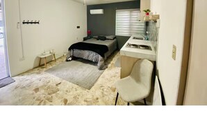 A bedroom with a bed, a desk, a chair, a ceiling fan, and a window.