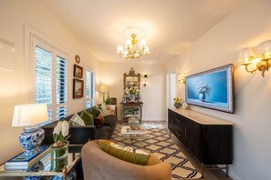 A living room with a sofa, a coffee table, a TV, a fireplace, and a chandelier.