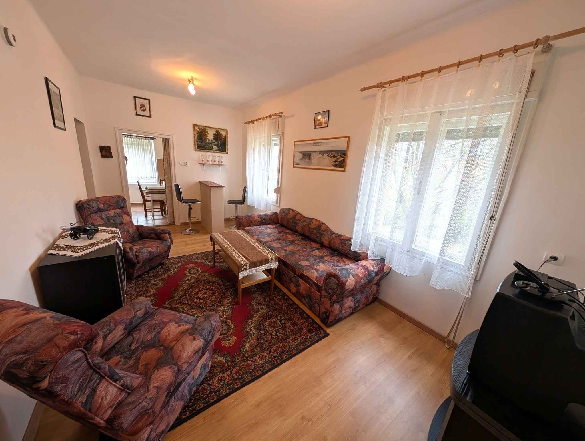 Ein Wohnzimmer mit einer Sofagarnitur, einem Couchtisch, einem Fernseher und einem Essbereich mit Stühlen und einem Tisch.