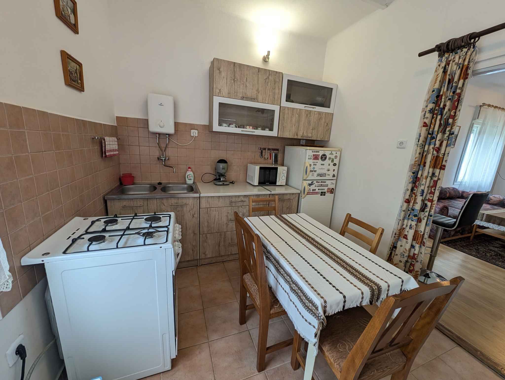 Une cuisine compacte équipée d’une cuisinière à gaz, d’un four à micro-ondes et d’un réfrigérateur, ainsi que d’une table à manger avec des chaises et d’une fenêtre avec des rideaux.