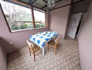 Ett rum med ett bord och stolar, ett fönster med utsikt över ett hus och en dörr som leder till ett annat rum.