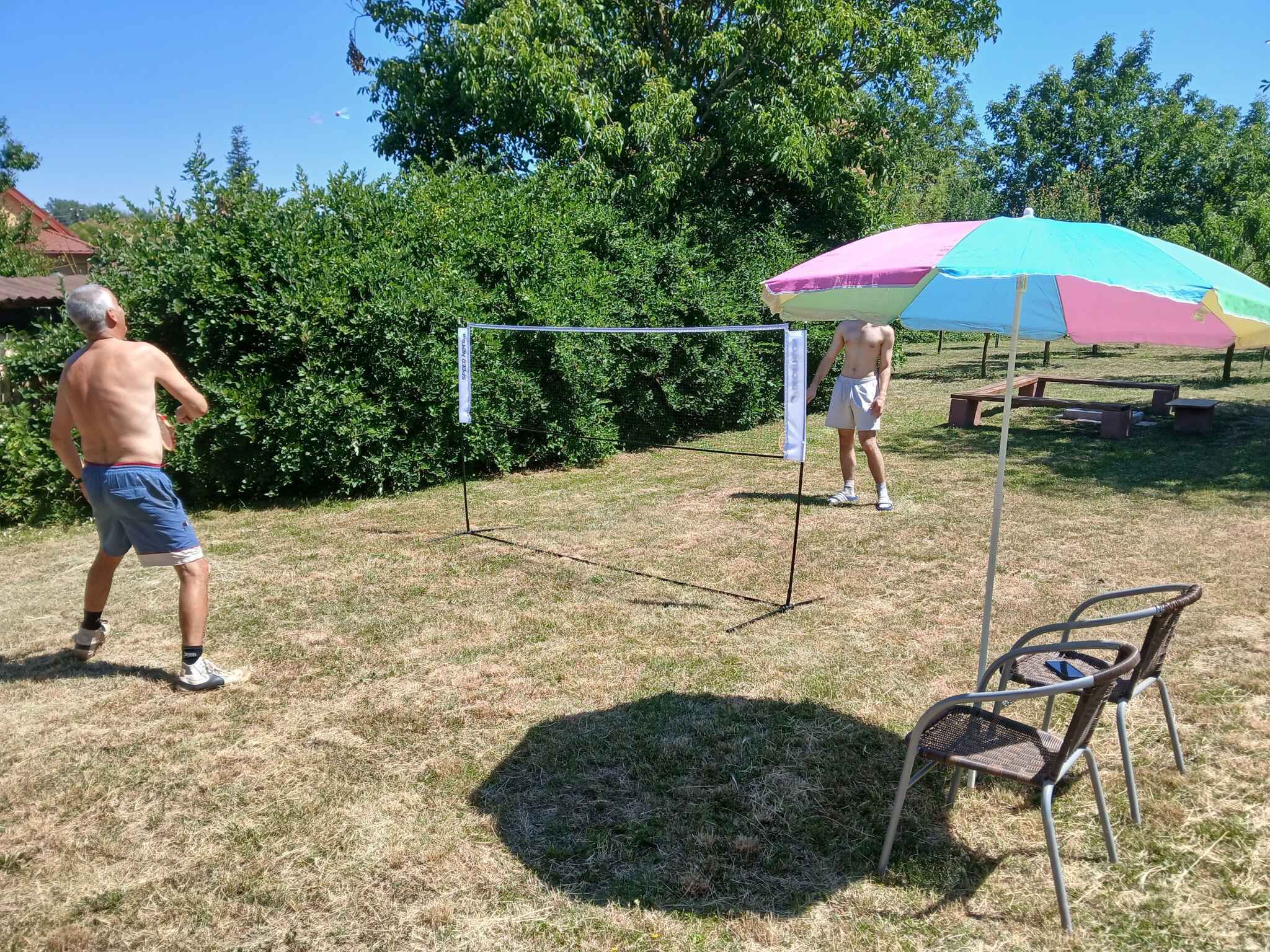 An outdoor area with a volleyball net, a picnic table, and a colorful umbrella.