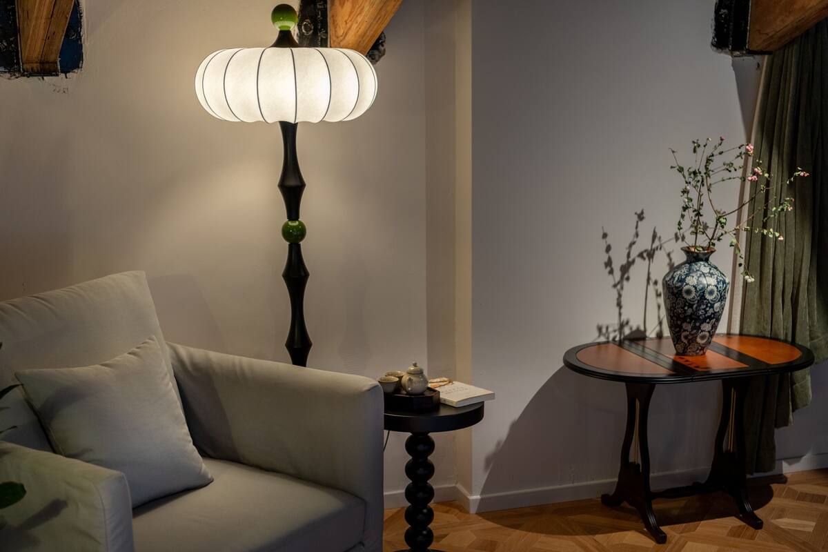 A room with a sofa, a table with a vase, a lamp, and a wooden ceiling.