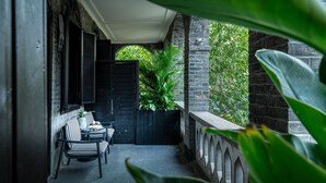 Un espace extérieur abrité, doté d’un mur en briques, d’une porte à volets noirs et d’un bac à fleurs rempli de verdure.