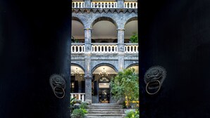 Une entrée d’immeuble avec une façade en pierre, des fenêtres en arc de cercle et un balcon doté de balustrades.