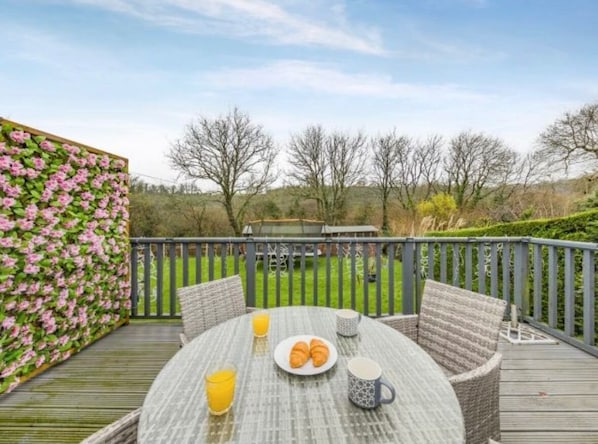 A round table with a plate of croissants and a glass of orange juice, surrounded by wicker chairs on a wooden deck.
