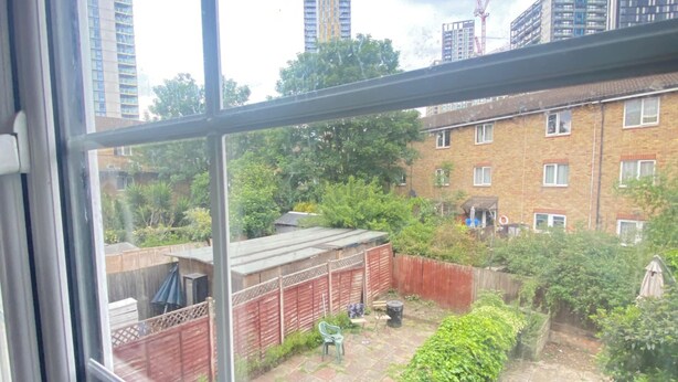 Uitzicht door een raam op een woongebied met een gebouw van baksteen, een omheind gazon en een groene stoel.
