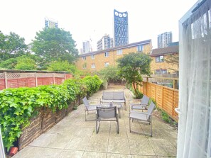 A patio with outdoor furniture, a wooden fence, and a view of tall buildings in the background. - London Luxe 5-Bed House Retreat (London)