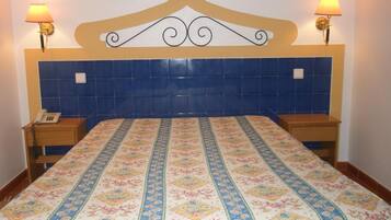 Una habitación de hotel con una cama, dos mesitas de noche, un teléfono y lámparas de pared.