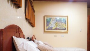 Un dormitorio con cabecera de madera, dos camas con ropa blanca, un cuadro de un leopardo en la pared y techo de madera.