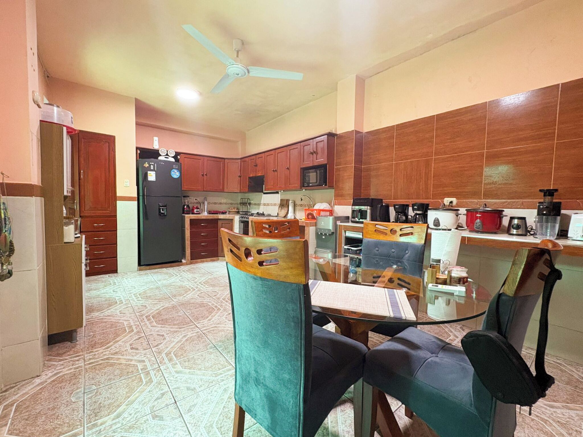 A compact kitchen with a refrigerator, microwave, and stove. There is a dining area with a glass table and chairs.