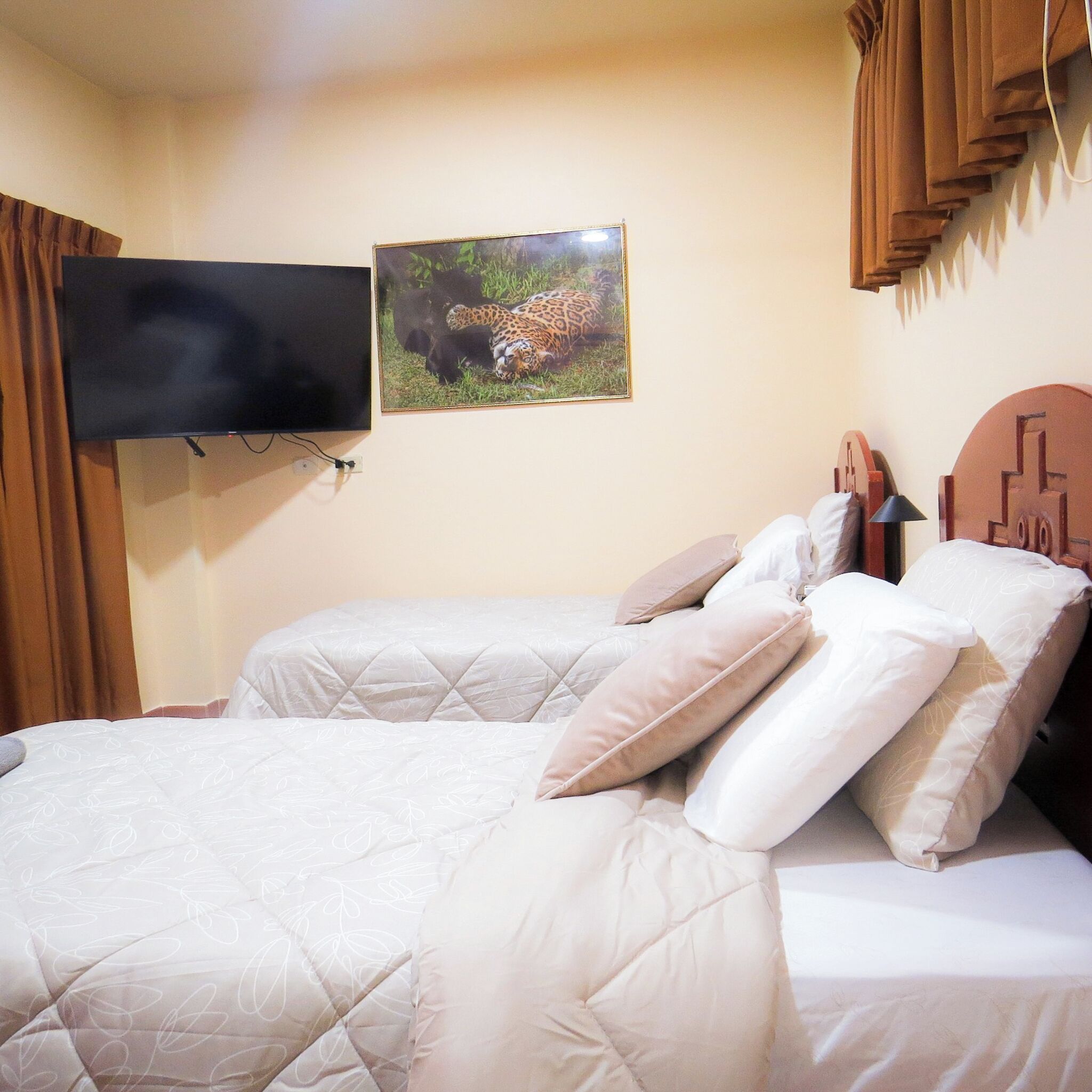 A hotel room with a bed, a television mounted on the wall, and a framed picture of a leopard.