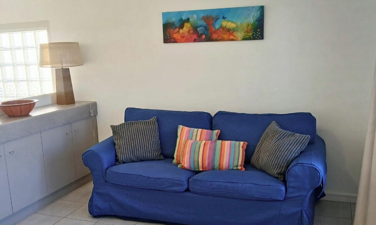 A blue sofa with striped and multicolored pillows, a lamp, and a painting on the wall.