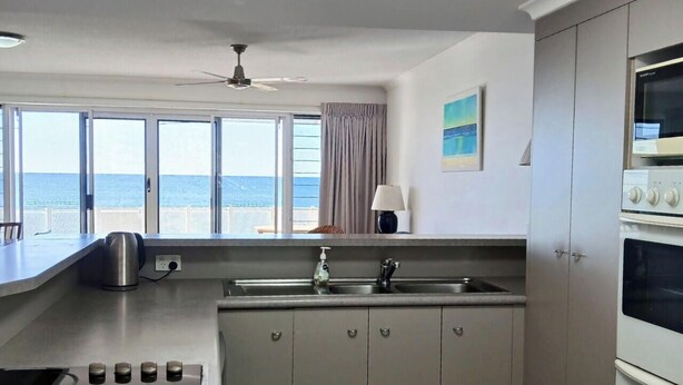 A kitchen with a view of the sea, a ceiling fan, and a microwave. - Above The Dunes (Woorim)