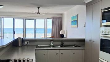 A kitchen with a view of the sea, a ceiling fan, and a microwave.