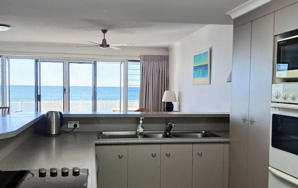 A kitchen with a view of the sea, a ceiling fan, and a microwave. - Above The Dunes (Woorim)