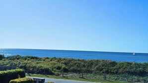 A coastal view with a clear sky, a body of water, and a distant sailboat. - Above The Dunes (Woorim)