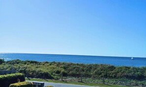 A coastal view with a clear sky, a body of water, and a distant sailboat. - Above The Dunes (Woorim)