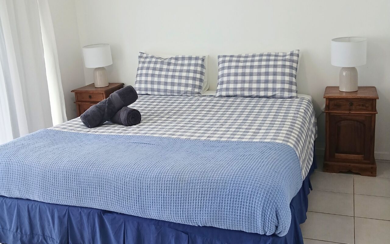 A bed with a checkered bedspread, two pillows, a blue blanket, and two bedside tables with lamps.