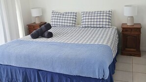A bed with a checkered bedspread, two pillows, a blue blanket, and two bedside tables with lamps. - Above The Dunes (Woorim)