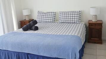 A bed with a checkered bedspread, two pillows, a blue blanket, and two bedside tables with lamps.