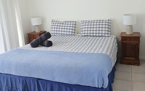 A bed with a checkered bedspread, two pillows, a blue blanket, and two bedside tables with lamps. - Above The Dunes (Woorim)