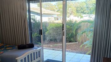 A room with a bed, a sliding glass door to a patio, and a view of a backyard with a wooden fence and greenery.