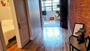 A hallway with wooden flooring, a sliding door, a small table with a plant, and a brick wall.