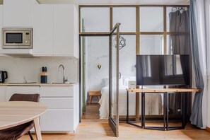 Ein kompakter Wohnbereich mit einer Küchenzeile, einem Essbereich, einem Fernseher auf einem Schrank und einer Schiebetür zu einem Schlafzimmer.
