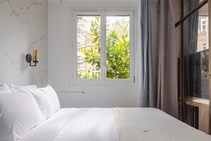 Ein Schlafzimmer mit Bett, einem Fenster mit Blick auf Grünflächen, einer Wandleuchte und einem dunkelbraunen Kleiderschrank.