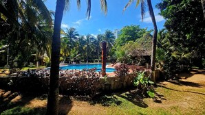 A pool surrounded by palm trees and greenery, with a clear blue sky. - 🌊 Condo in the Cancun Hotel Zone | Just Steps from Playa Ballenas and the Mall (Cancún)