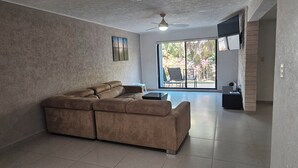 A living room with a sectional sofa, a ceiling fan, and a large window with a view of outdoor furniture. - 🌊 Condo in the Cancun Hotel Zone | Just Steps from Playa Ballenas and the Mall (Cancún)