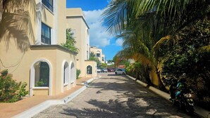 A narrow street lined with buildings, parked cars, and palm trees. - 🌊 Condo in the Cancun Hotel Zone | Just Steps from Playa Ballenas and the Mall (Cancún)