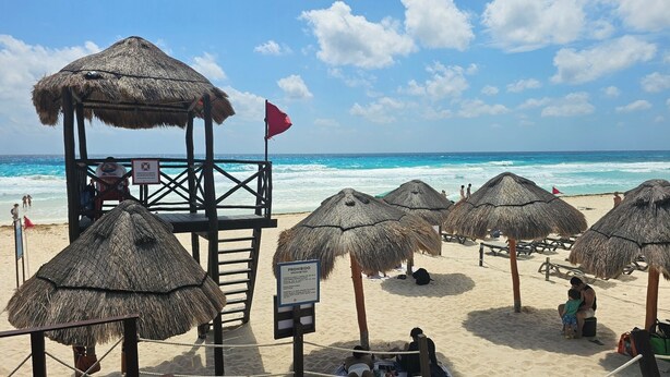 A beach with thatched umbrellas, a lifeguard tower, and a clear view of the ocean. - 🌊 Condo in the Cancun Hotel Zone | Just Steps from Playa Ballenas and the Mall (Cancún)