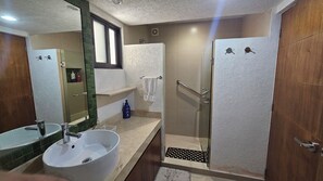Ein Badezimmer mit Waschbecken, Spiegel, Dusche und Handtuchhalter.