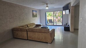 A living room with a sectional sofa, a ceiling fan, and a large sliding glass door leading to a balcony with plants. - 🌊 Condo in the Cancun Hotel Zone | Just Steps from Playa Ballenas and the Mall (Cancún)