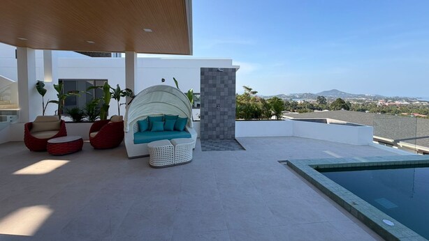 Ein moderner Außenbereich mit Sitzgelegenheiten, einem Pool und Blick auf die Stadt unter blauem Himmel.