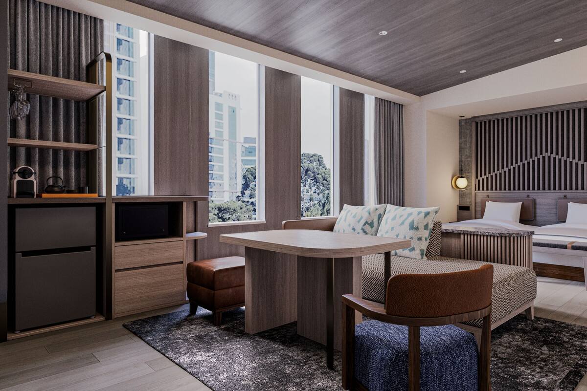 Una habitación de hotel moderna con un ventanal grande, una cama, un escritorio y un área de descanso.