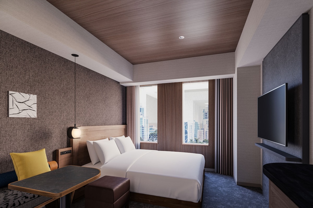 Una habitación de hotel moderna con cama, escritorio, silla, televisor y vista a la ciudad.