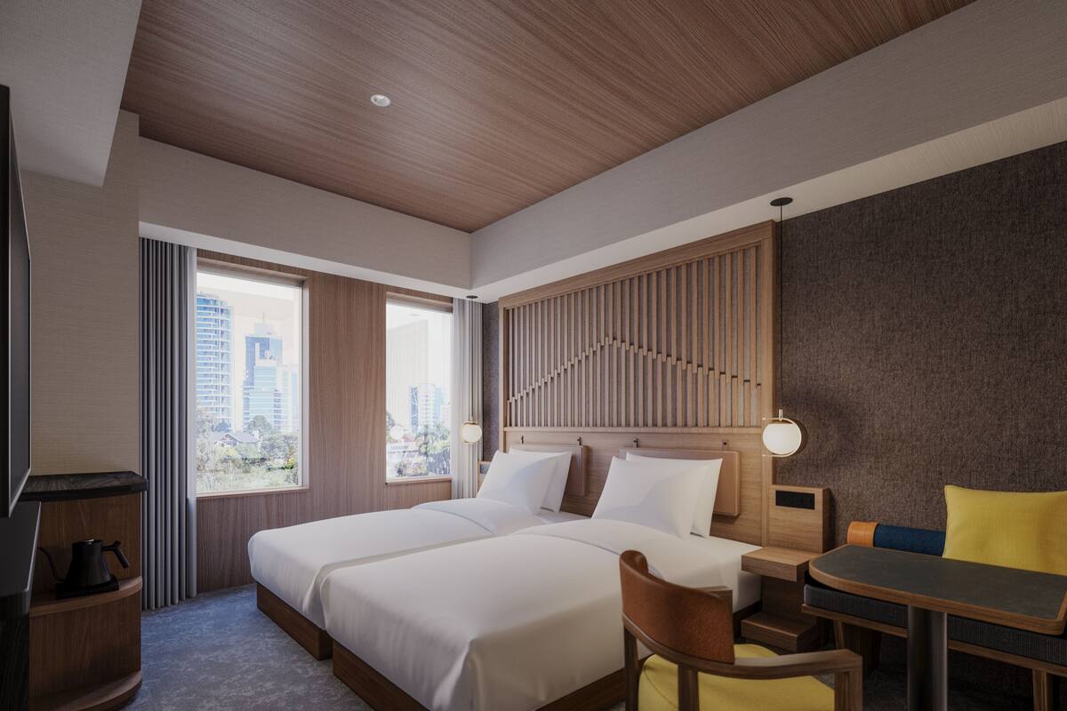 Habitación de hotel con dos camas, un escritorio, una silla, un televisor y vista a la ciudad.